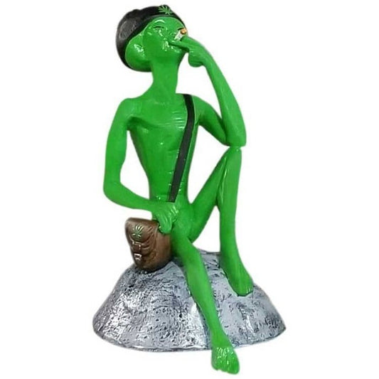 Green alien statue smoking, sitting on rock base, quirky yard decor