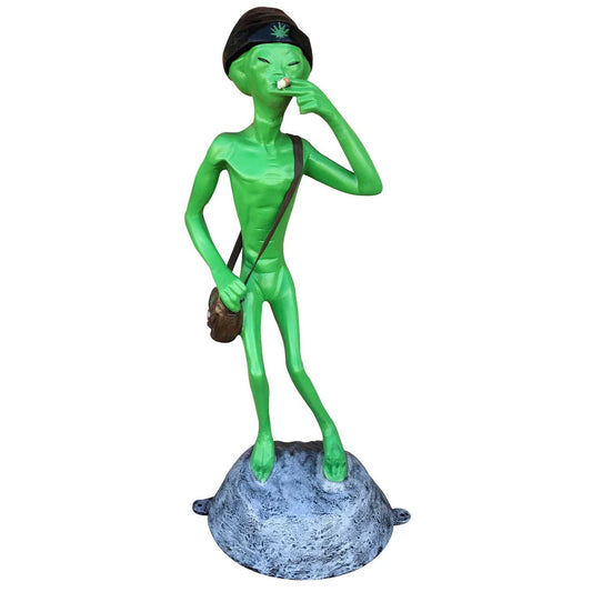 Green alien statue wearing beanie, holding joint, standing on rock base for yard decor