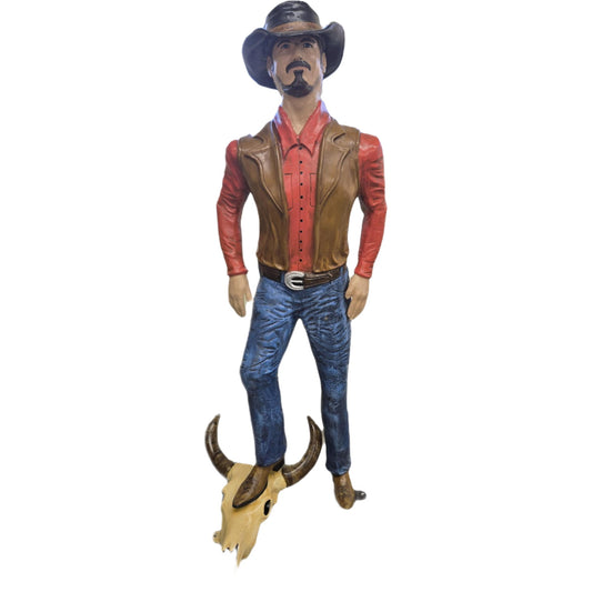 Cowboy statue in hat, red shirt, vest, standing on bull skull for yard decor
