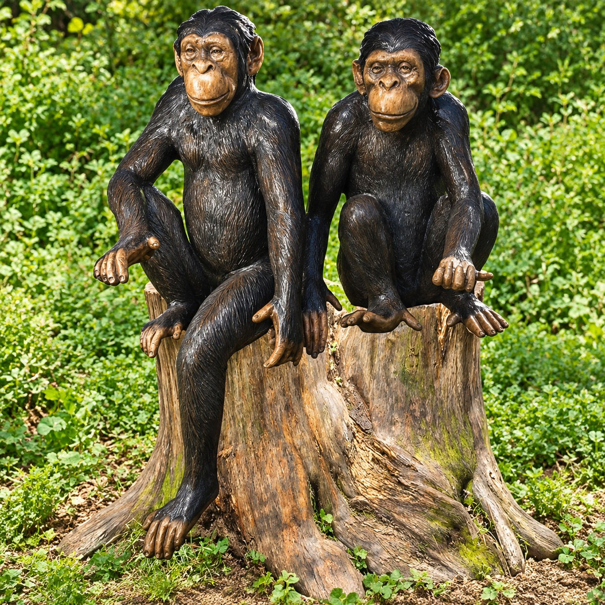 Two realistic monkey garden statues sitting on a weathered tree stump, photographed outdoors in a lush green garden setting.