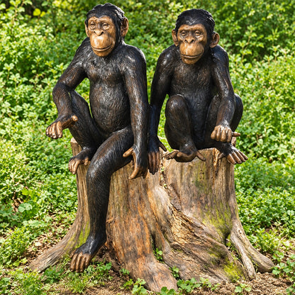 Two realistic monkey garden statues sitting on a weathered tree stump, photographed outdoors in a lush green garden setting.