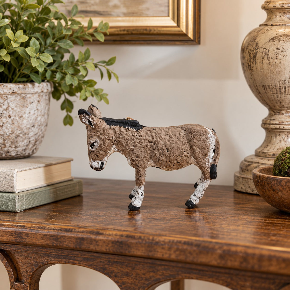 A small decorative cast aluminum donkey with a textured brown and beige body, black mane and tail, and white hooves, displayed on a wooden console table in a home decor setting.