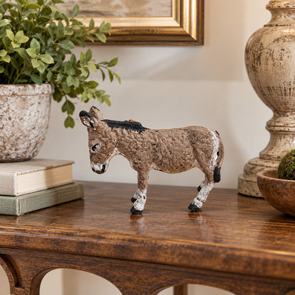 A small decorative cast aluminum donkey with a textured brown and beige body, black mane and tail, and white hooves, displayed on a wooden console table in a home decor setting.