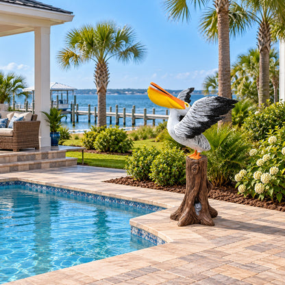 A decorative pelican garden statue perched on a tree stump, placed beside a swimming pool in a landscaped backyard with palm trees, shrubs, and a waterfront view.